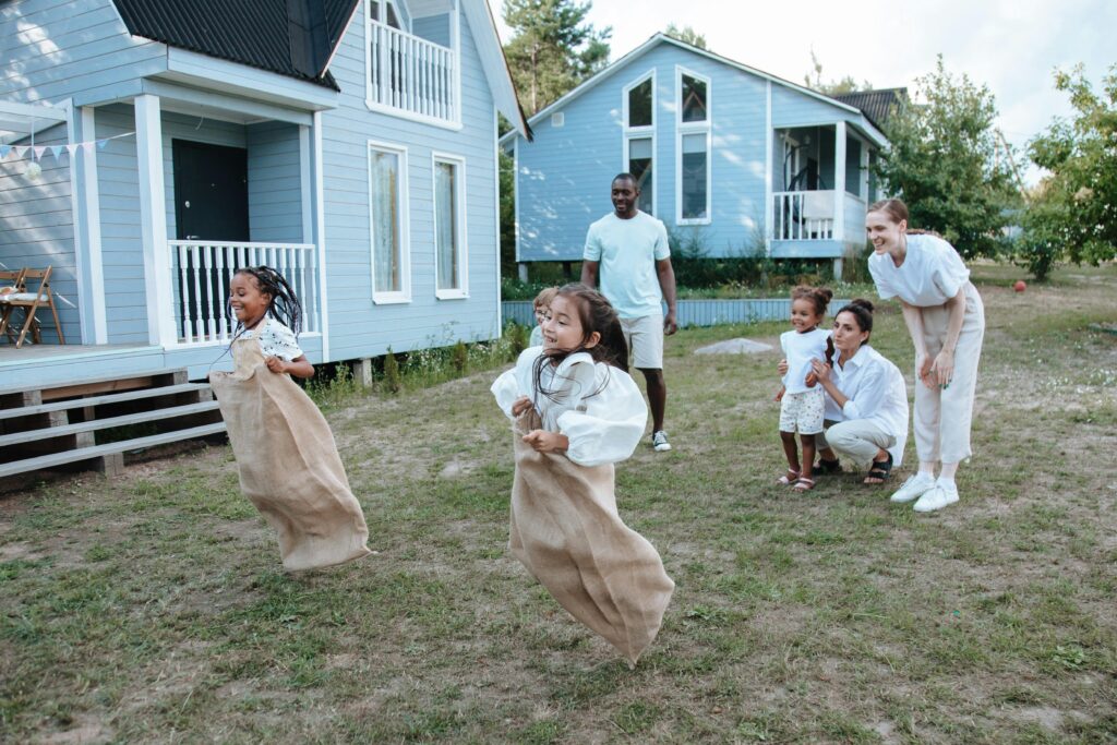 Group of children enjoying a sack race in a backyard setting, surrounded by family.